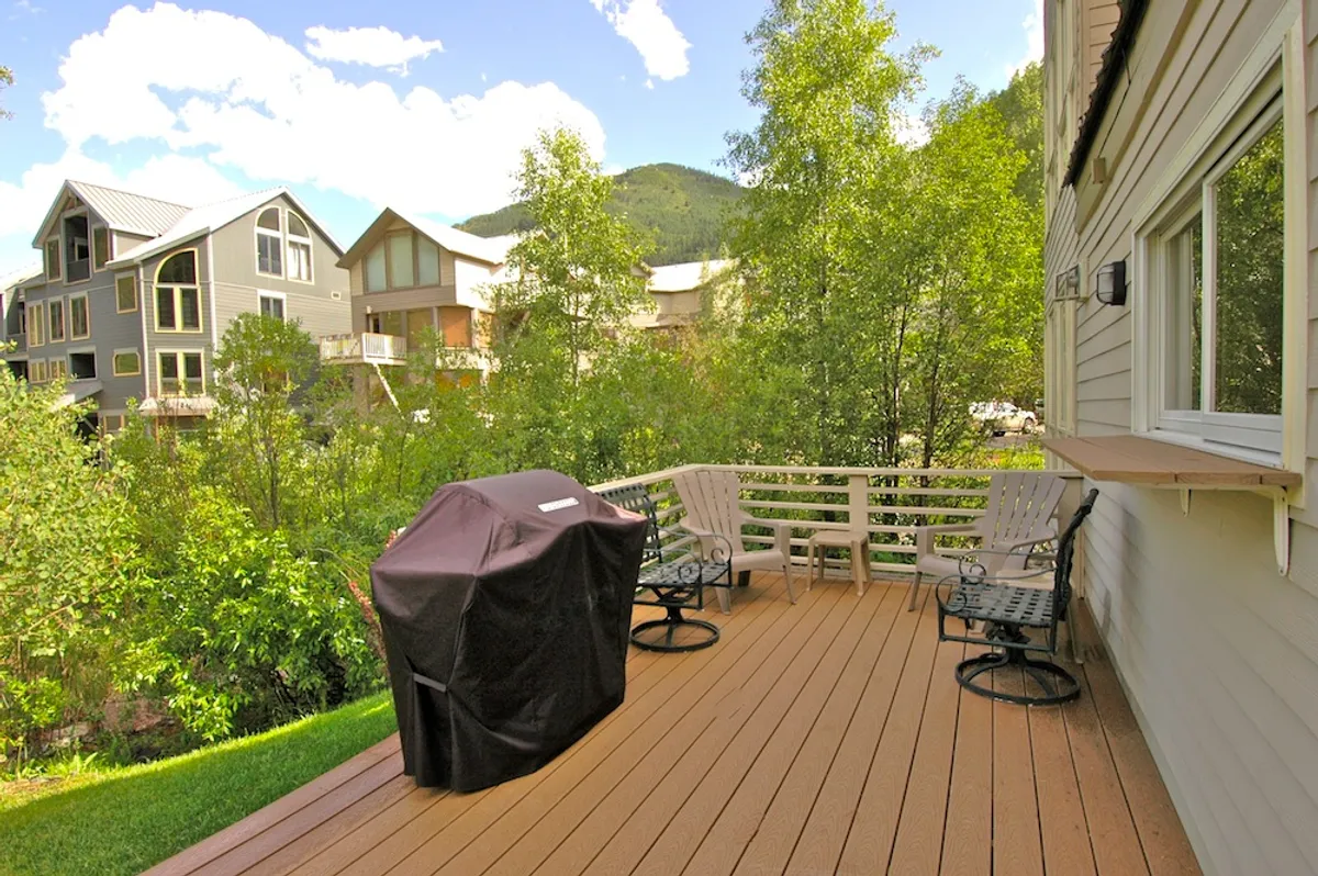 A relaxed wooden deck equipped with a grill, surrounded by trees and mountains. The deck is set up for outdoor dining and leisure, capturing the essence of barbecuing or enjoying a quiet moment in nature.