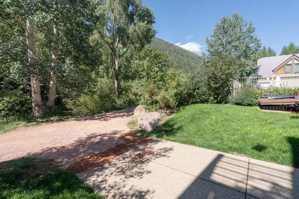 A vibrant, well-maintained lawn bordered by trees and mountains, featuring a gravel pathway where families can walk or picnic. The lush greenery and open space provide a peaceful, safe environment for children to run, play, or enjoy nature with their families.