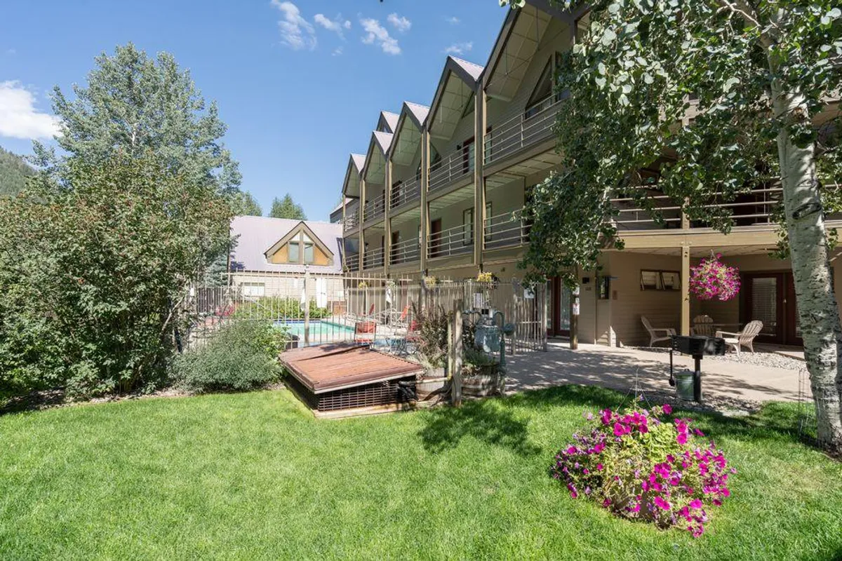 A swimming pool surrounded by flower beds and adjacent to balconies, indicating a resort-style outdoor amenity. The space evokes relaxation, sunbathing, and community gatherings, in a setting integrated with nature.