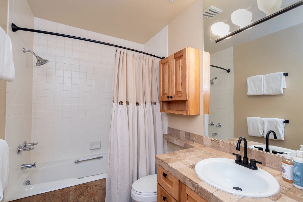 A stylish bathroom with a bathtub, sink, and wooden cabinetry, all in a serene and inviting atmosphere. The space is designed for relaxation and personal care, perfect for unwinding after a busy day.